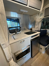 Inside this RV rental, a compact travel trailer kitchen: sink, stovetop, microwave, and fridge, with a cozy dinette.