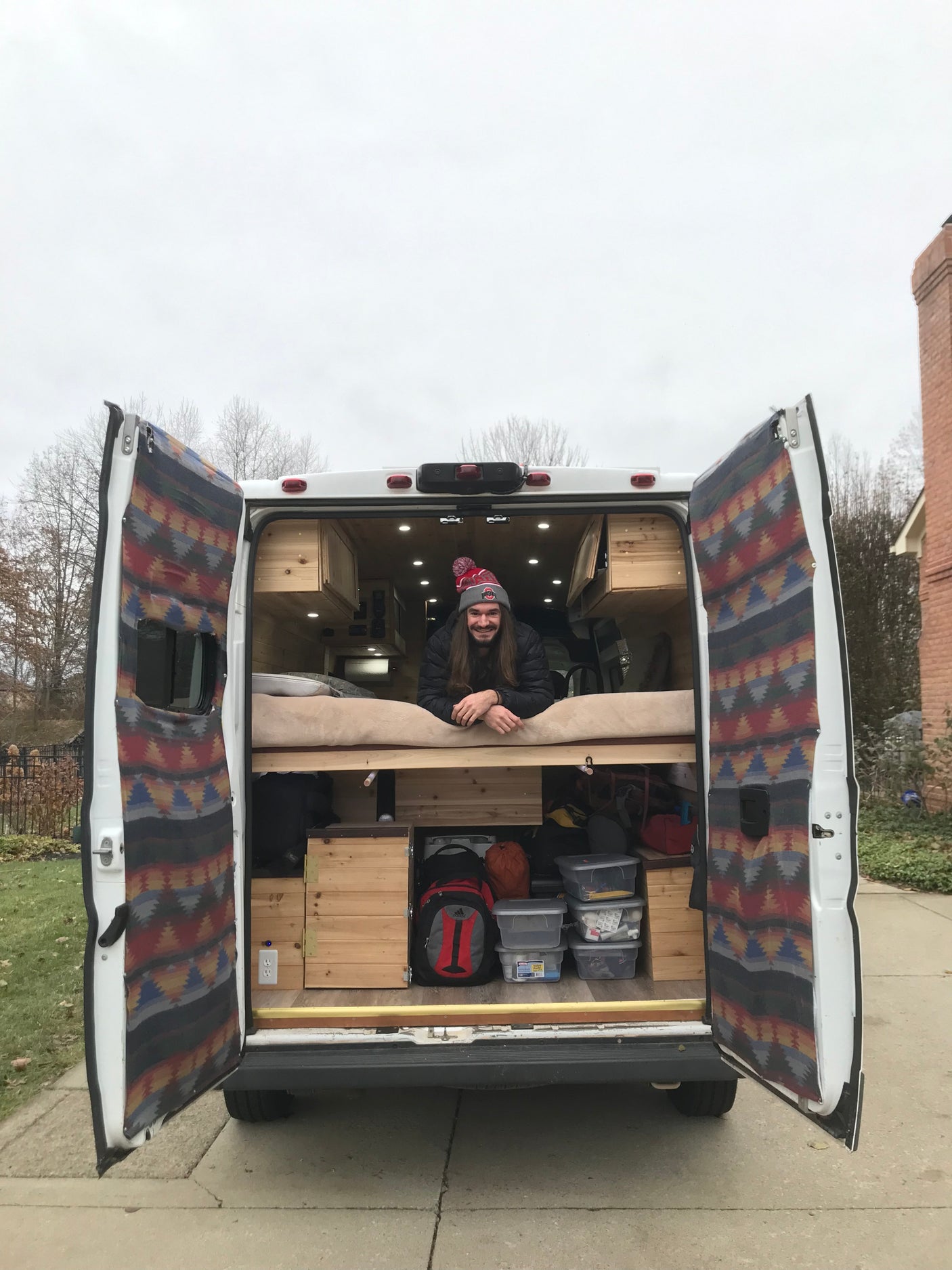 Explore van life! Man smiles from his customized camper van, featuring a bed & storage – great for RV rental.