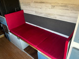 Comfortable red bench seating with storage in an RV rental's living area, featuring wood-look walls and a laminate floor.