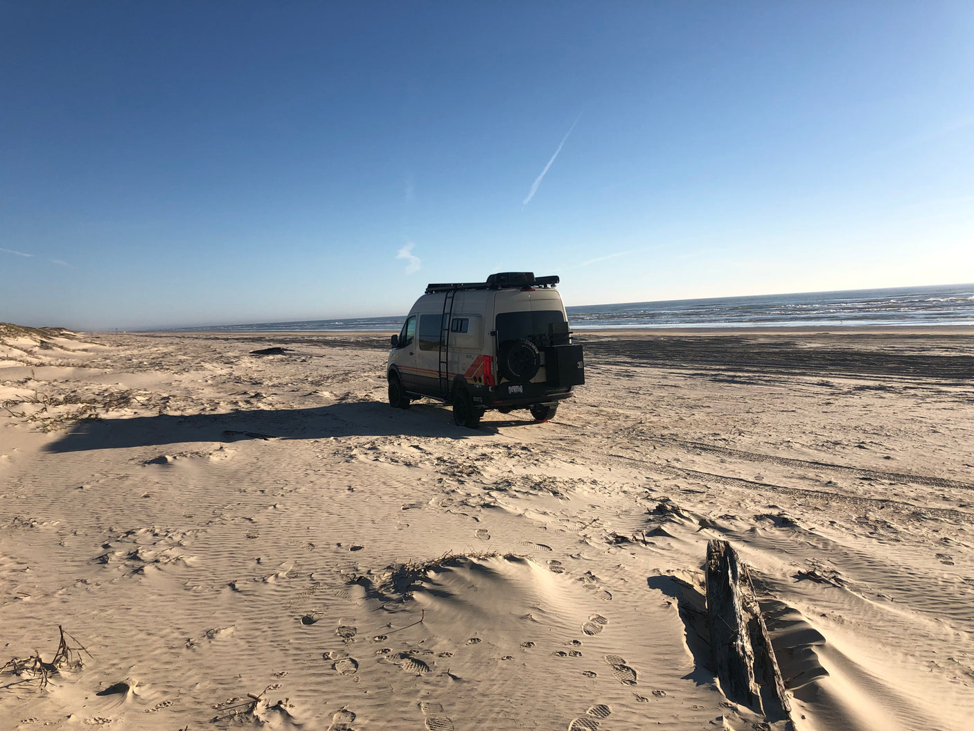 A sleek camper van, ideal for an rv rental, is parked on a sunny, expansive beach, with ocean waves in the distance.