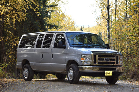 Silver Ford E-Series RV rental van on an autumn road in Alaska, surrounded by vibrant fall colors.