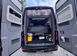 Rear of an RV rental with open doors revealing interior storage, a yellow box, and a white bottle in a door pocket.