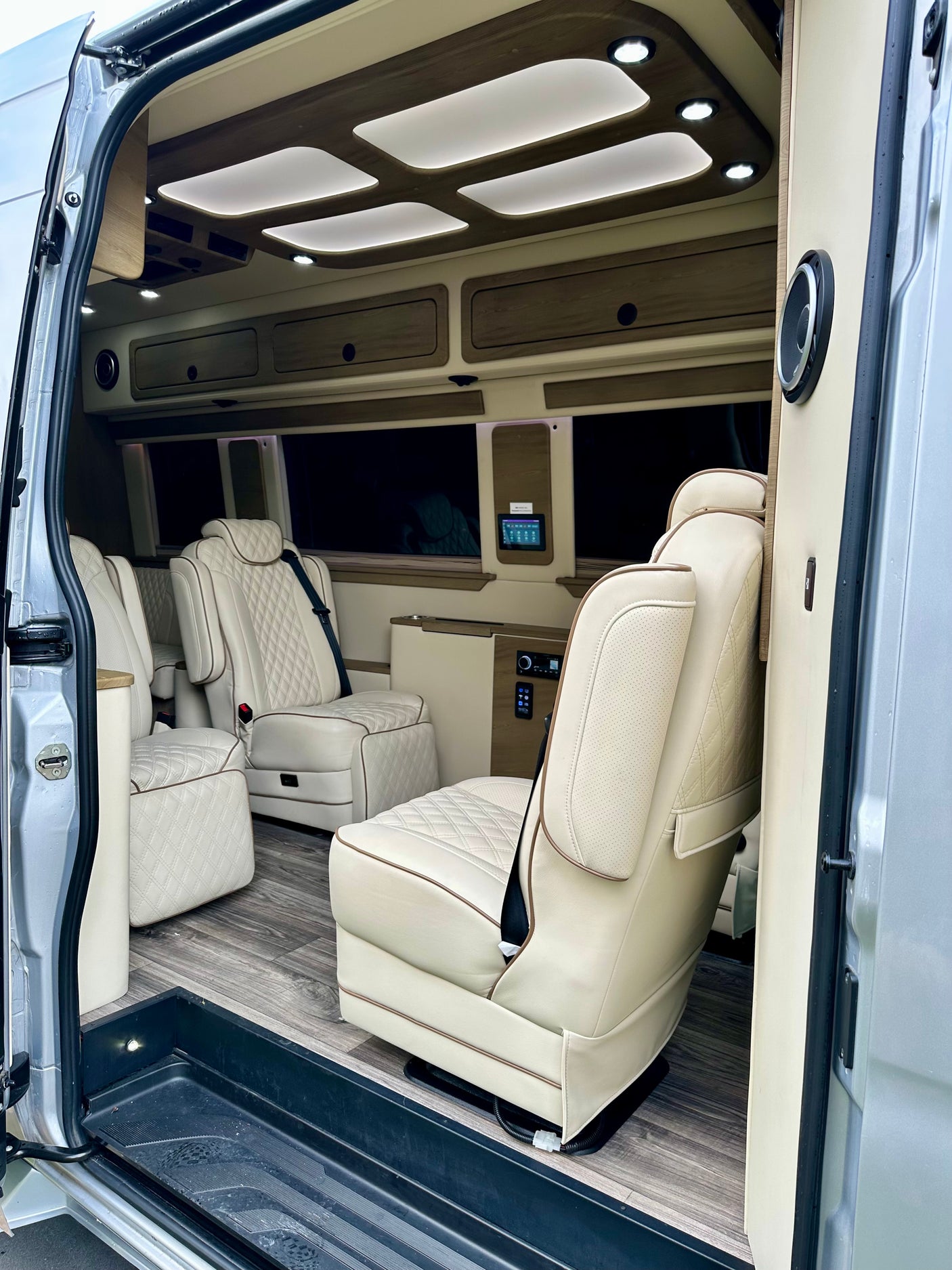 Step into this plush rv rental interior with quilted cream leather seats, sleek wood flooring, and modern LED lighting from the open side door.