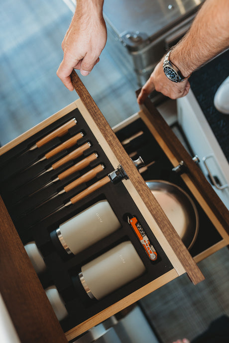 Accessing a custom-fitted drawer in an RV rental, revealing organized steak knives, Purist bottles, and a multi-tool.
