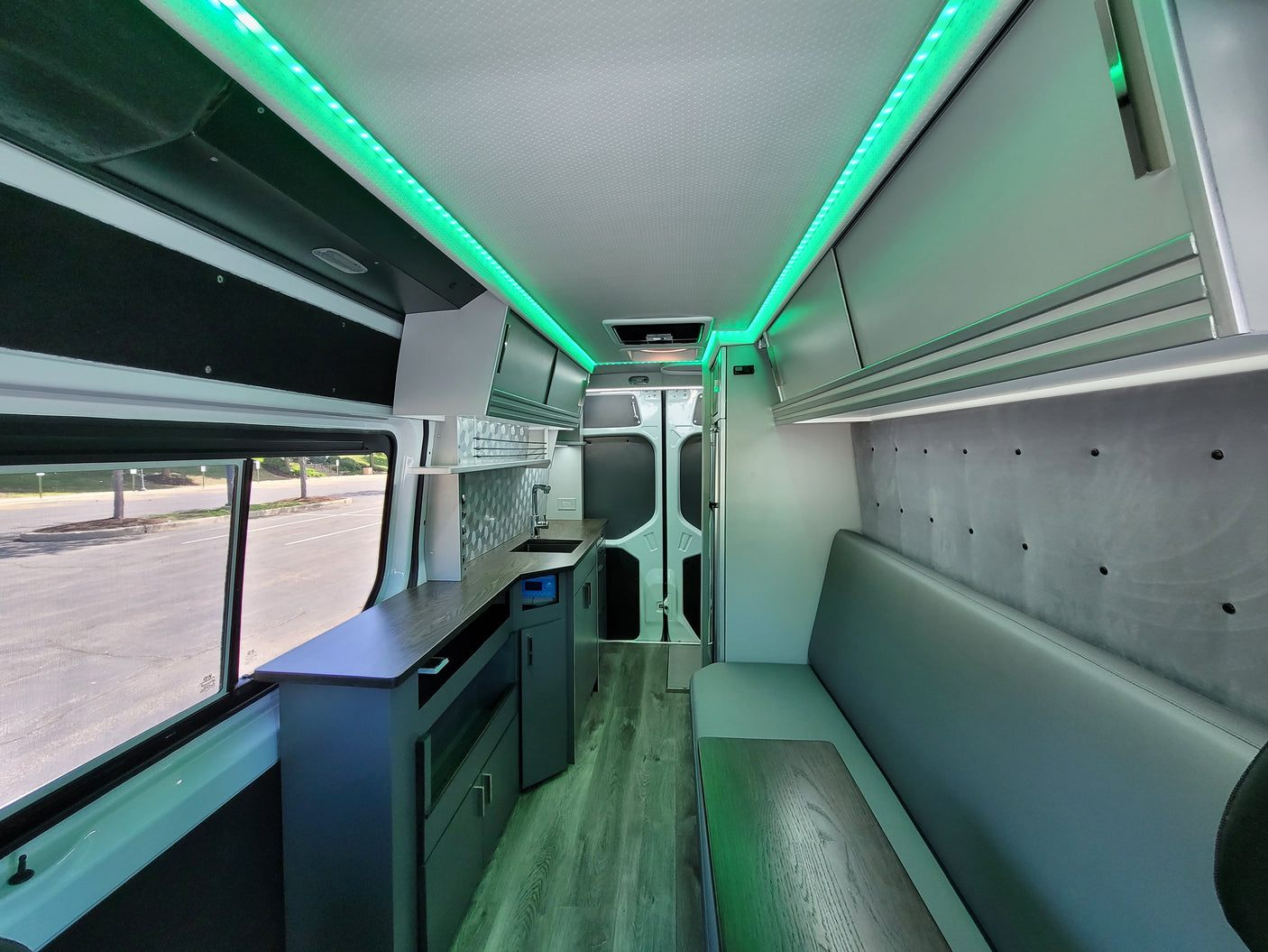 This modern rv rental interior features vibrant green LED lighting, a functional kitchenette, and comfortable seating with a table.