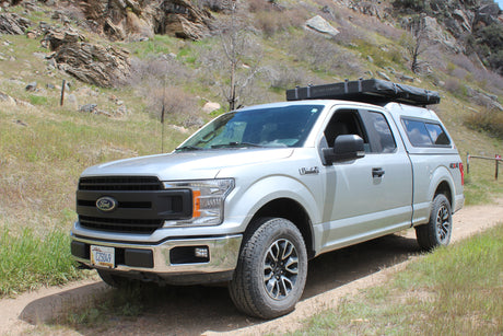 This Ford F-150 truck with a roof tent and camper shell on a dirt road offers a unique RV rental adventure.