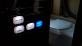 RV rental control panel with illuminated light buttons and a blue Speakers button, positioned next to a toilet.