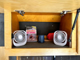 RV rental: Inside a wooden cabinet, two portable fans, a Sony speaker, and a "Colorado's Hot Springs" book are neatly stored.