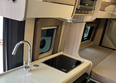 RV rental: A compact RV kitchen with a chrome faucet, sleek stovetop, overhead microwave, and a plush sleeping area.