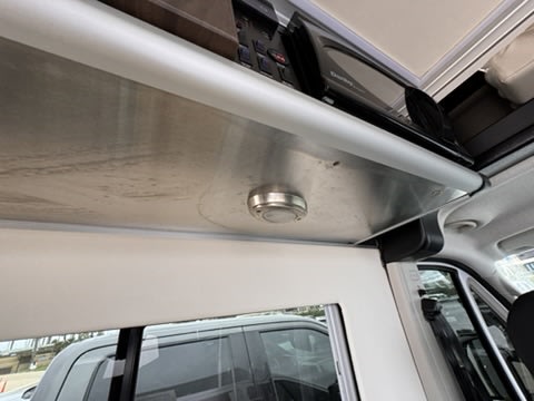 RV rental camper van interior featuring an overhead microwave, integrated light, and metal shelf above a window.