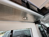 RV rental camper van interior featuring an overhead microwave, integrated light, and metal shelf above a window.