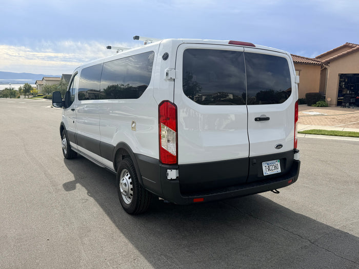 White Ford Transit rv rental van with roof racks & Montana plate, parked on a street with houses and hills in background.