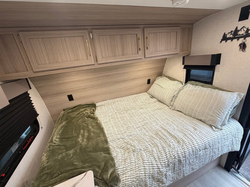 and dog with toy at a sunny pine forest campsite with a small campfire.|This inviting RV rental bedroom features striped bedding — photo 8