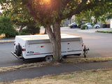 A white Coleman Sedona pop-up RV rental, parked under a sunny tree for your next outdoor adventure.