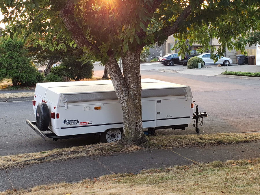 A white Coleman Sedona pop-up RV rental, parked under a sunny tree for your next outdoor adventure.