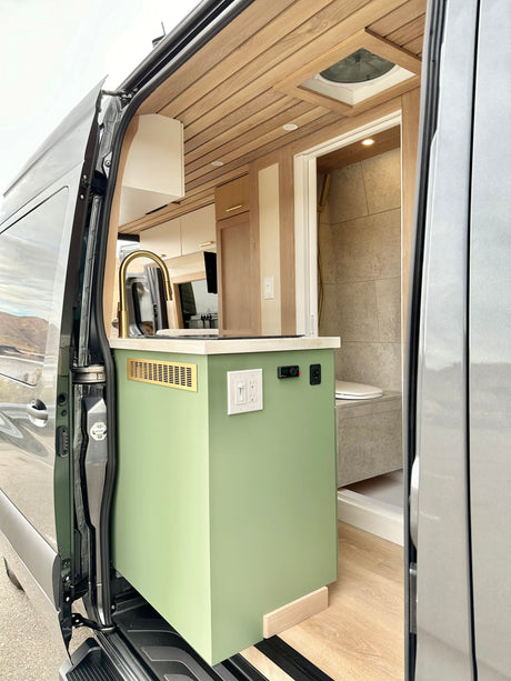 View inside an **rv rental**, showing a sage green kitchen with gold faucet & a compact shower/toilet area.