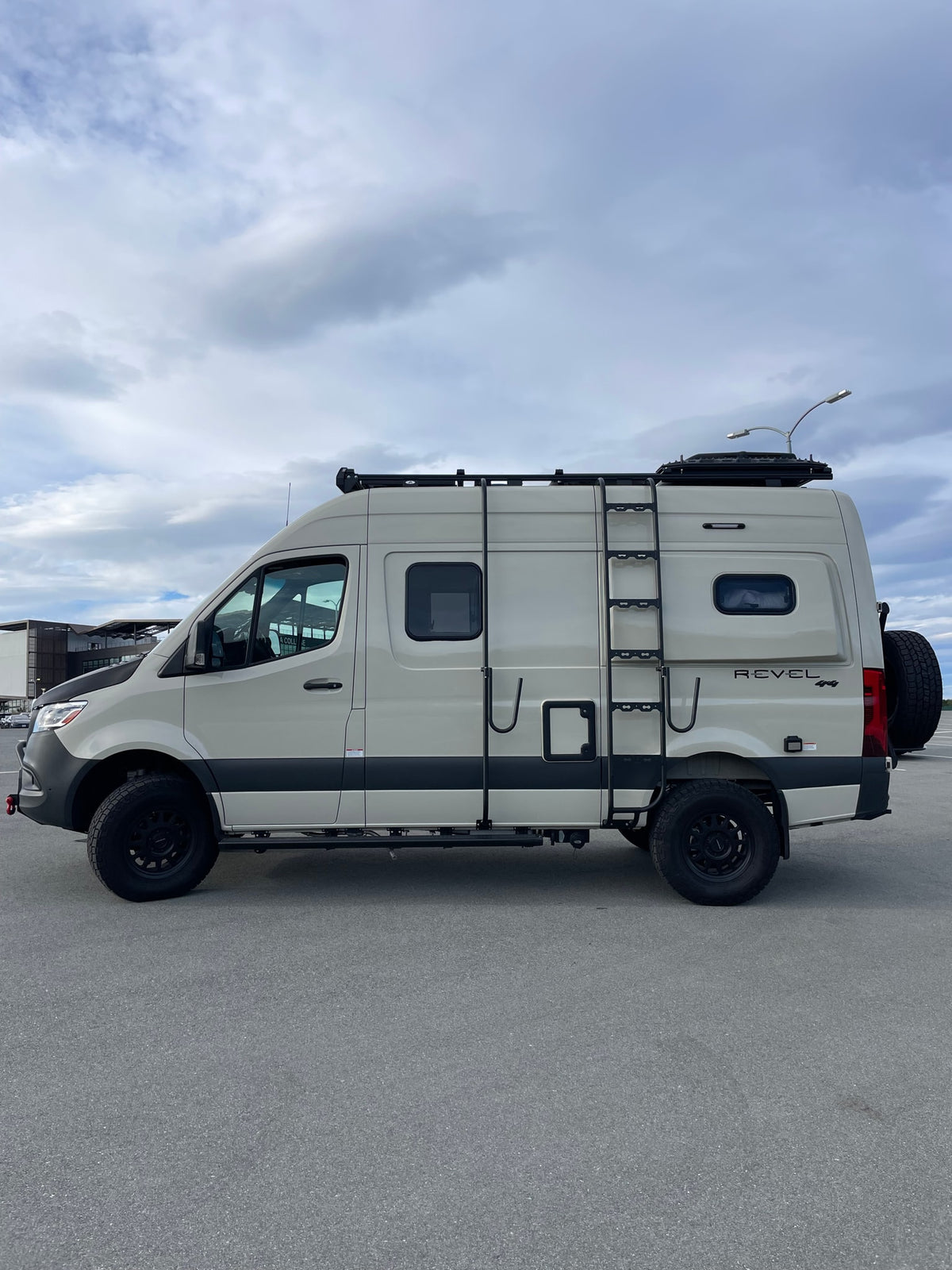 This beige Sprinter RV rental, equipped for off-road adventure with a roof rack and ladder, is parked on asphalt. — photo 3