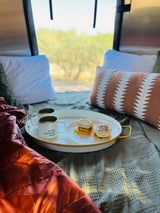 Breakfast in an RV rental: two mugs, two sandwiches on a tray with comfy pillows & outdoor views. Let the adventure begin!