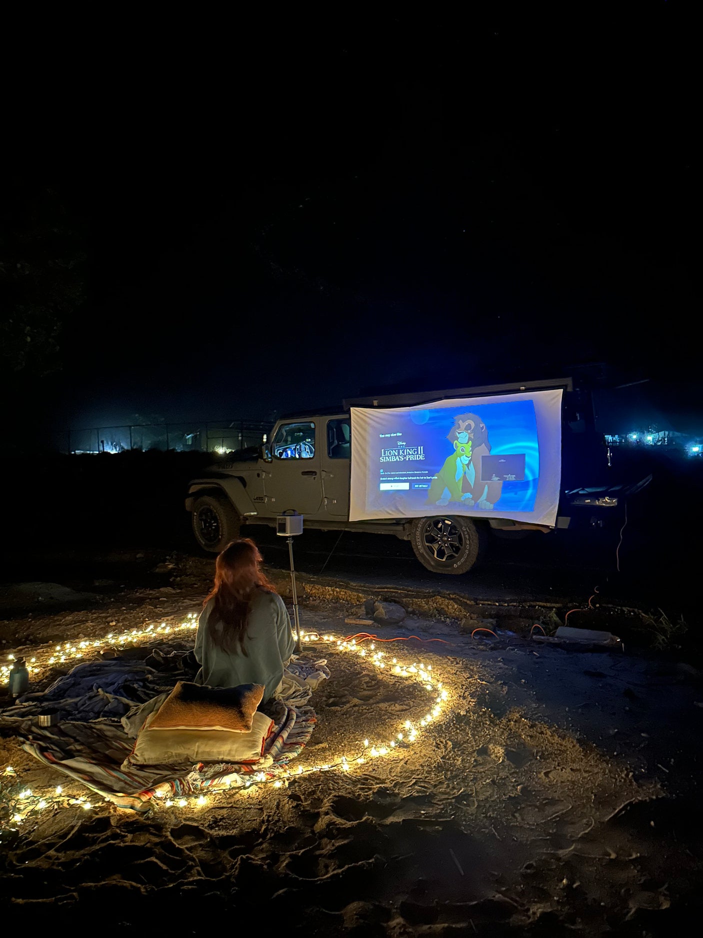 Outdoor movie night, projecting The Lion King 2 from a Jeep onto a screen, with string lights. Great for an RV rental trip!