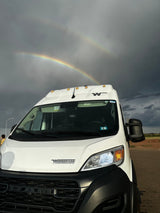 White Winnebago camper van RV rental under a stunning double rainbow in a stormy sky