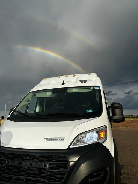 White Winnebago camper van RV rental under a stunning double rainbow in a stormy sky