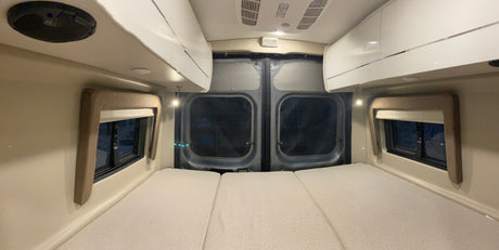 Inside an RV rental: a cozy sleeping area with three laid-out mattresses, side windows, and overhead cabinets.