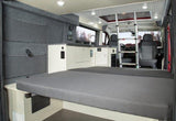 Modern rv rental interior showing a comfortable bed, galley kitchen, front cabin, and overhead ladder for adventure.