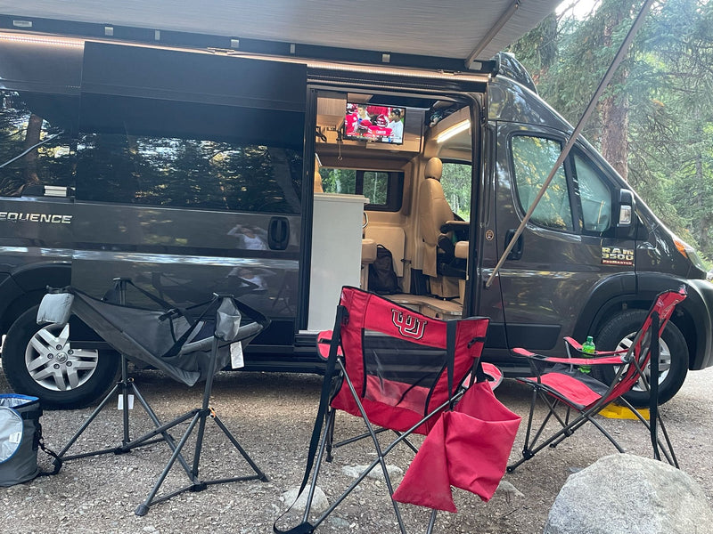 RV rental camper van with awning out at a gravel campsite. Red chairs (Utah Utes!) are set up, and a TV plays inside. — photo 7