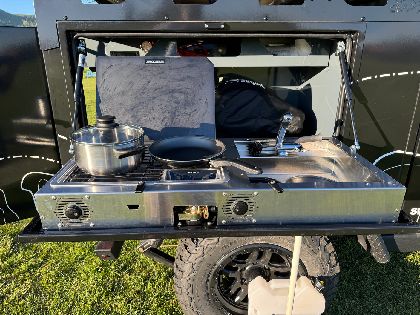 RV rental outdoor kitchen: a pull-out unit with stove, sink, pot, and pan, perfect for camping cooking.