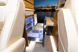 Luxurious RV rental interior with an open, illuminated pull-out refrigerator, wood cabinetry, and a scenic water view.