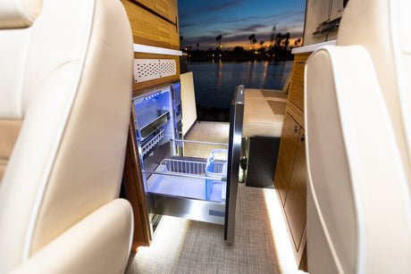 Luxurious RV rental interior with an open, illuminated pull-out refrigerator, wood cabinetry, and a scenic water view.
