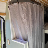 RV rental: Light-colored privacy curtain on track inside a camper van, with wall-mounted switch visible.