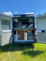 This RV rental campervan's open rear doors reveal a bed & organized storage, perfect for your next outdoor adventure in nature.
