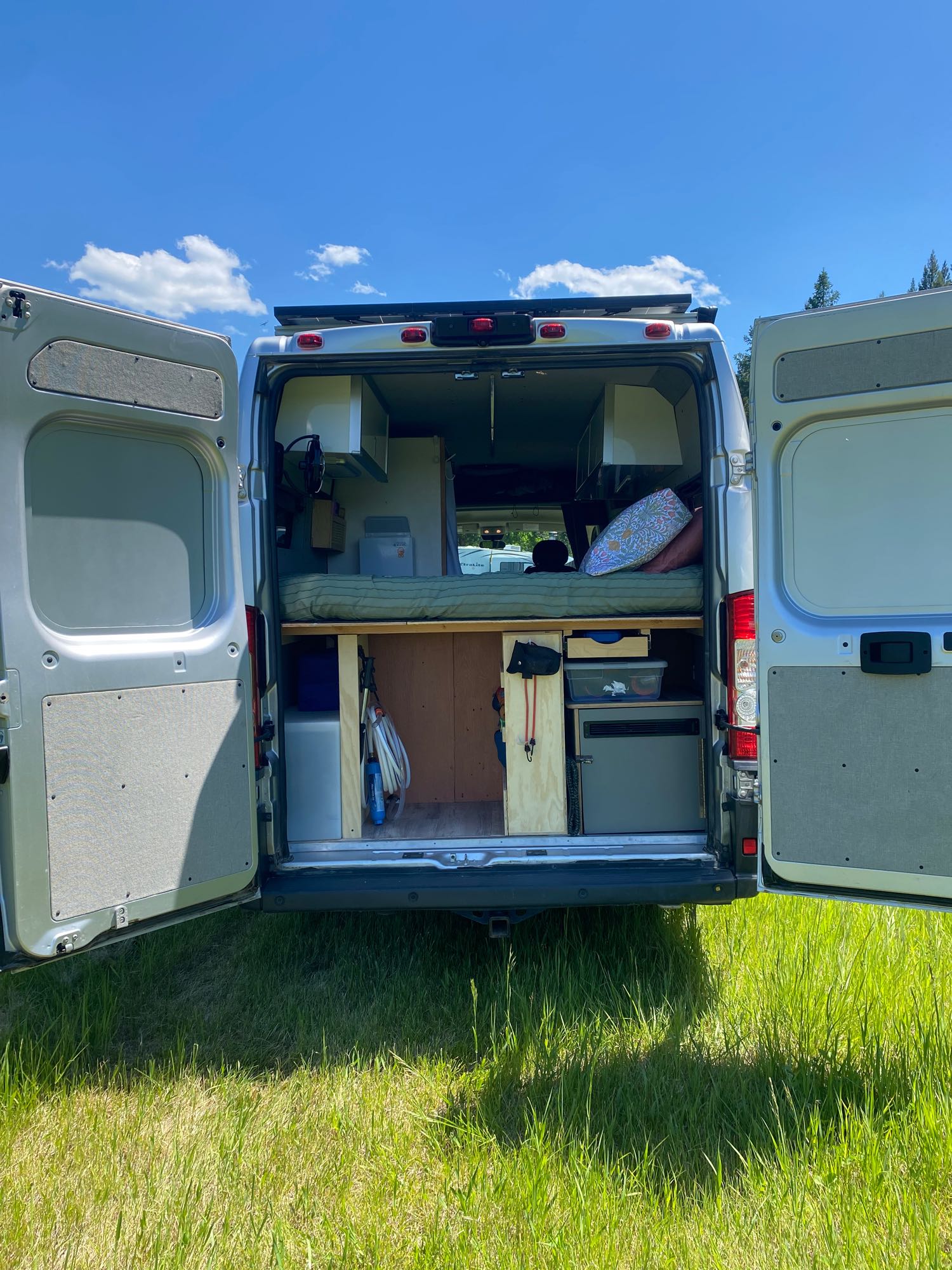 This RV rental campervan's open rear doors reveal a bed & organized storage, perfect for your next outdoor adventure in nature.