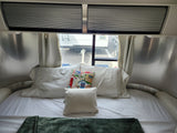 Inside a comfortable rv rental: a cozy bedroom with a white bed, colorful pillow, and window views.