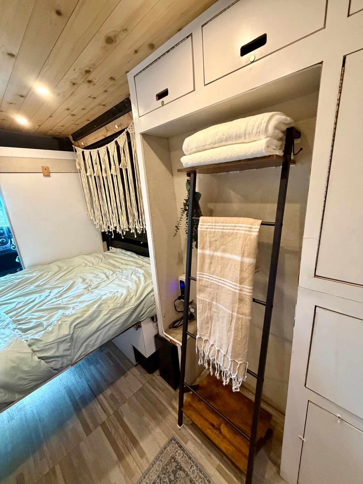 This rv rental boasts a cozy bed, wood plank ceiling, white storage cabinets, and a decorative towel display.