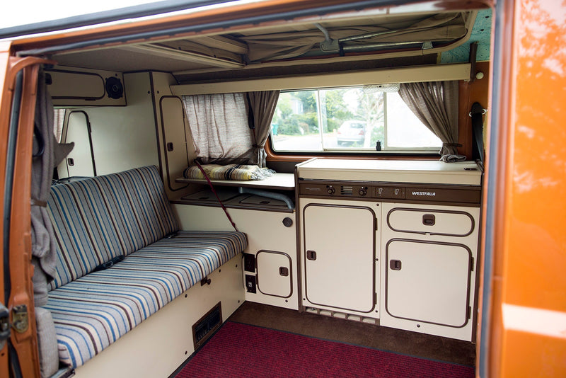 Step inside this classic Westfalia RV rental! Features striped seating, a compact kitchenette, and cozy living space. — photo 3