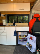 RV rental: a cozy converted van interior with a compact kitchen, open fridge, and a window view.
