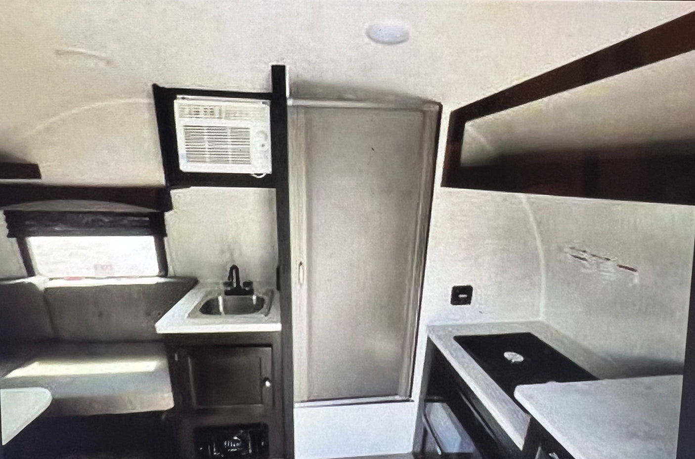 RV rental: Inside view of a compact camper kitchen with sink, window AC, dinette, and bathroom door.