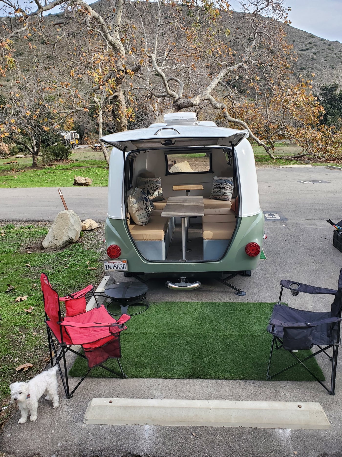 Compact teardrop RV rental with open hatch revealing seating, setup for camping with outdoor chairs and a small dog. — photo 20