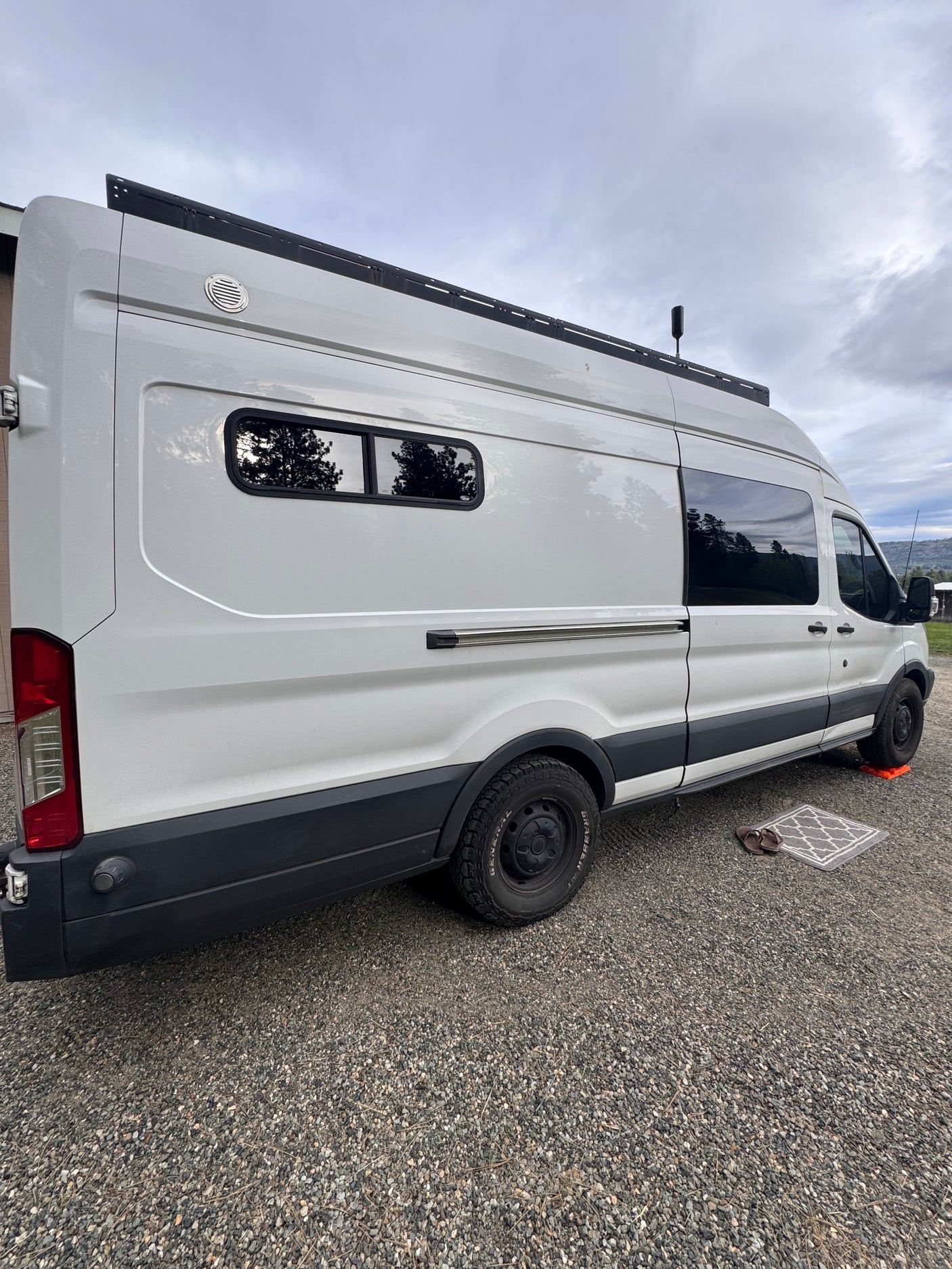 Side view of a white Ford Transit camper van parked on gravel, suggesting an RV rental ready for adventure.
