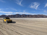 Explore vast deserts in a yellow Jeep with a rooftop tent, ideal for an RV rental adventure. Mountains and clear skies complete the scene.