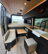Step inside this custom RV rental camper van! A modern interior with wood accents, kitchen, bed, dining, and ocean view awaits.