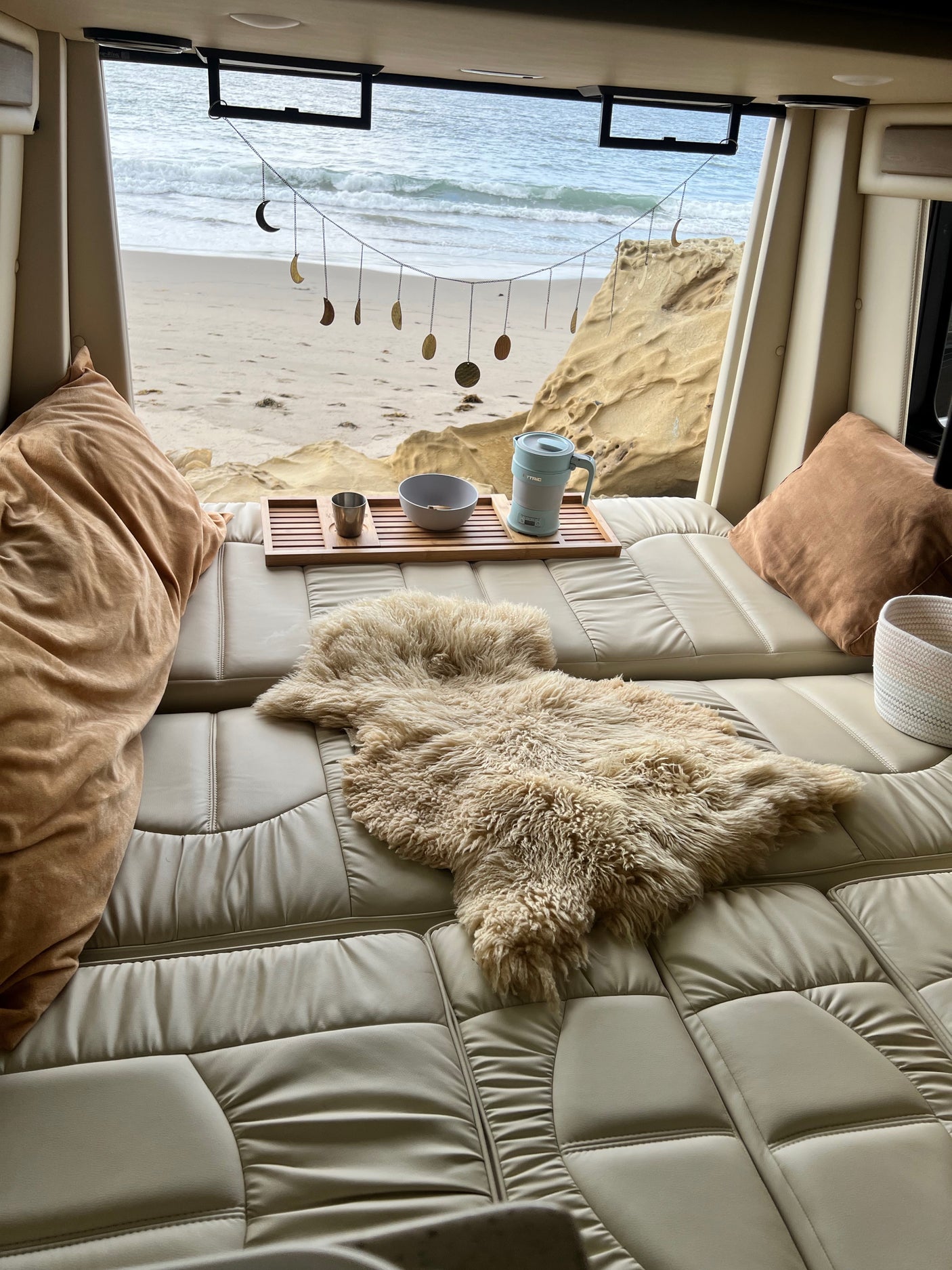 Relax in this RV rental's comfy cream bed, featuring a cozy rug, drinks tray, and charming moon phase decor with a beach view.