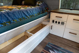 Clever storage in this cozy RV rental! An under-bed compartment is open, beside white cabinets with controls.