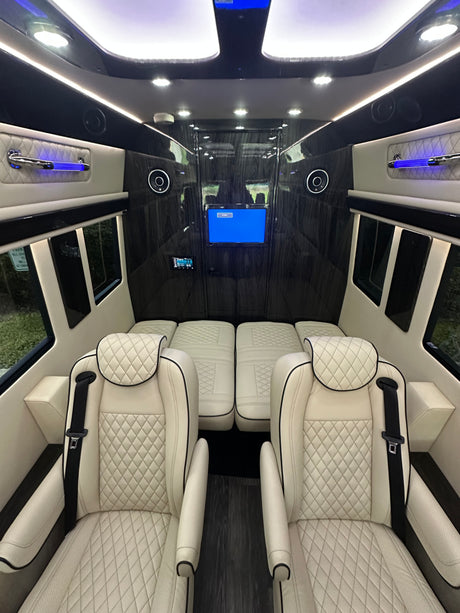 Plush RV rental interior: white quilted seats, entertainment screen, and wood accents create a luxurious lounge.
