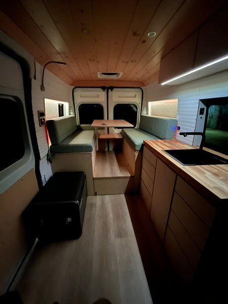 Discover this cozy RV rental's camper van interior, featuring a dinette, kitchen, & ambient lighting.