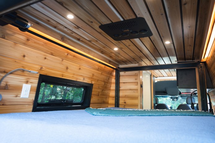 Cozy wood interior of an RV rental, showing the bed, window, and overhead lighting/AC for comfortable mobile living.