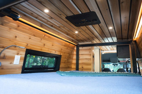 Cozy wood interior of an RV rental, showing the bed, window, and overhead lighting/AC for comfortable mobile living.