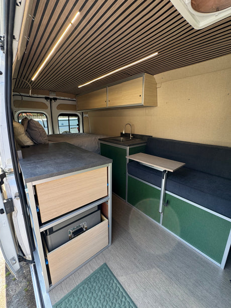 Stylish RV rental: This camper van features a wood-slat ceiling, full bed, kitchen, and dinette with table.